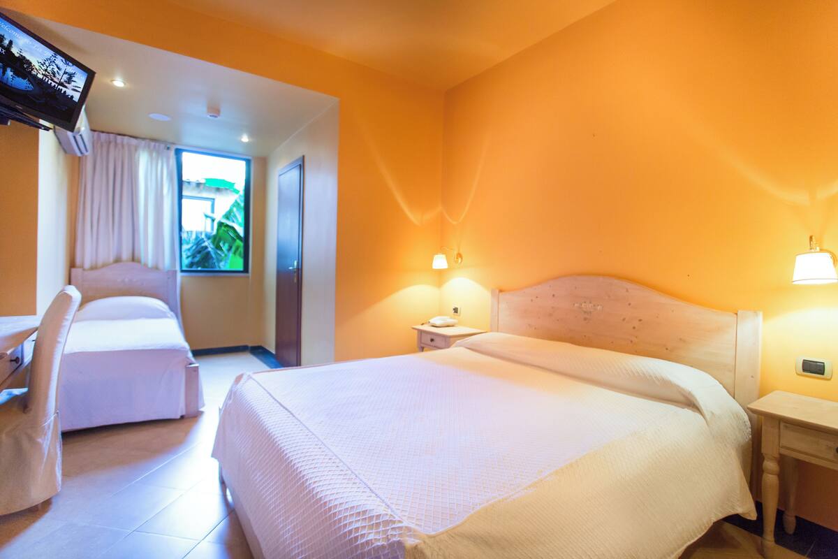 Ein Hotelzimmer mit einem großen Bett, einem Sessel, einem Fernseher und einem Fenster mit Vorhängen.