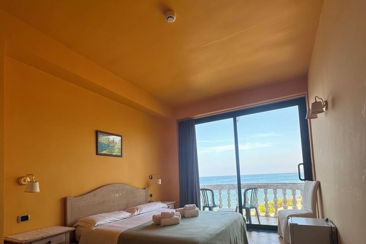 Ein Hotelzimmer mit zwei Betten, einem Balkon mit Meerblick, einem kleinen Tisch und einem Stuhl.