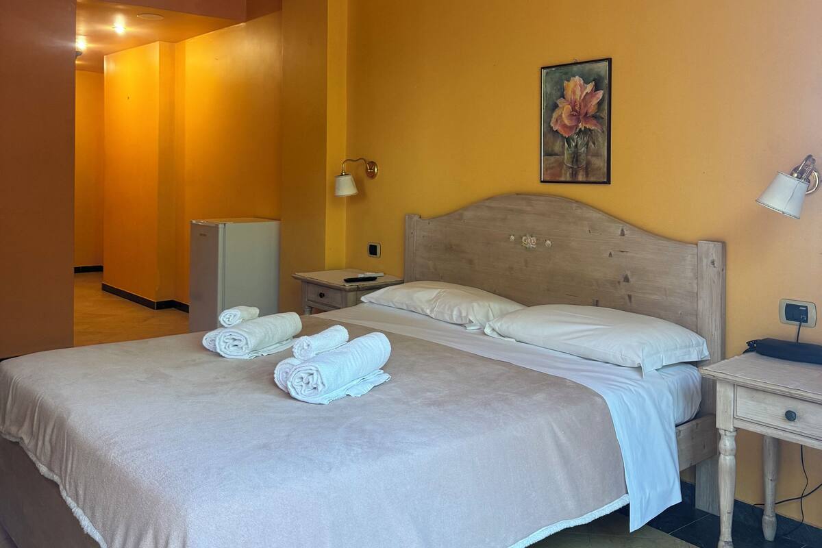 Ein Hotelzimmer mit Bett, Nachttisch, Lampe, Klimaanlage und einem Gemälde an der Wand.
