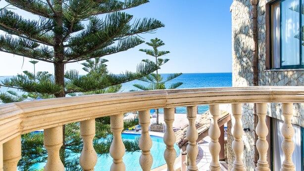 A poolside view with a stone balustrade, a large pine tree, and a clear view of the sea.