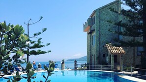 A swimming pool with clear blue tiles, surrounded by lounge chairs and a stone building with a tiled roof.