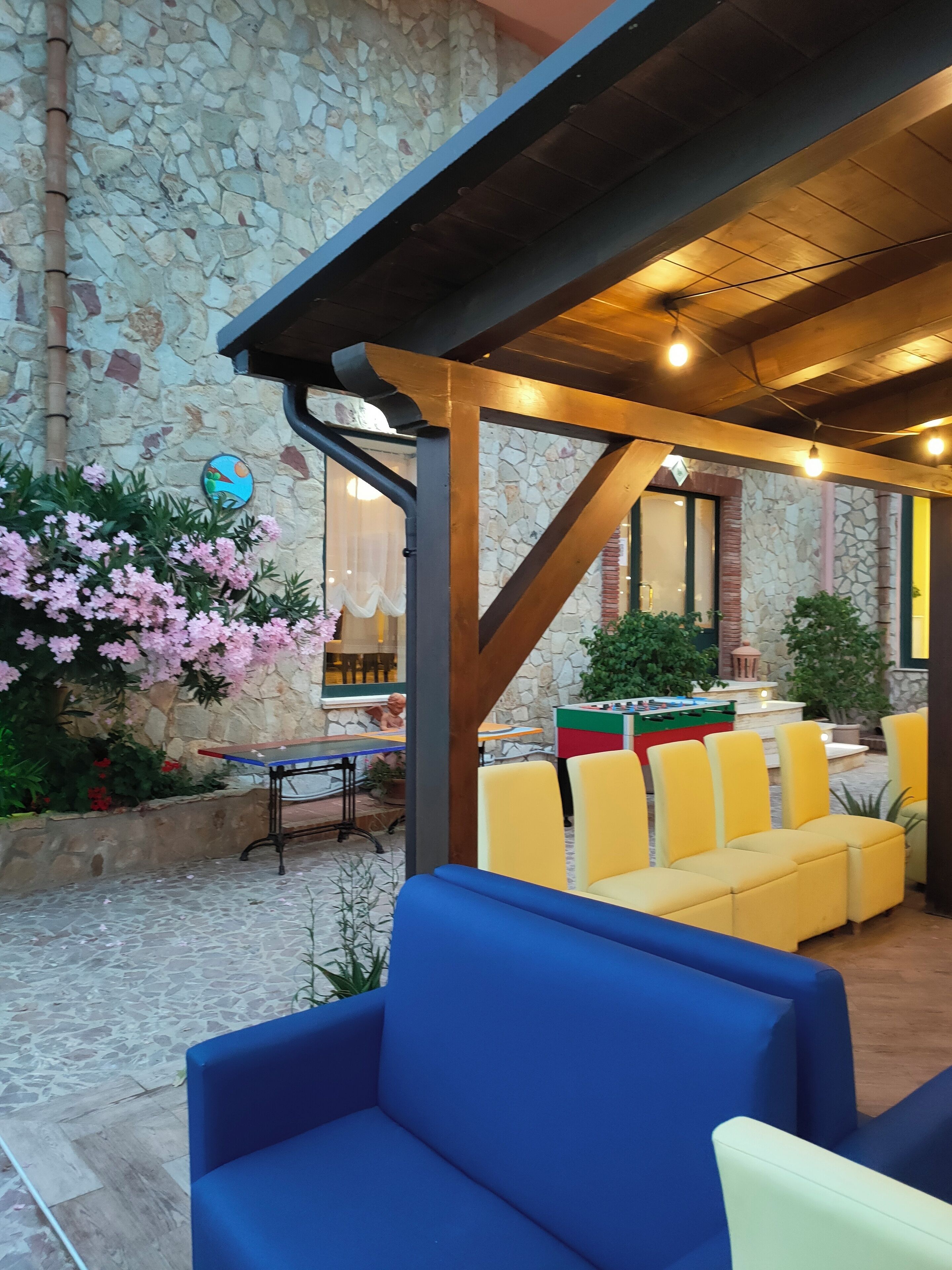 A covered outdoor seating area with blue and yellow chairs, a stone wall, and a foosball table.