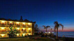 A hotel with multiple balconies, a pool area, and a view of the ocean at dusk.