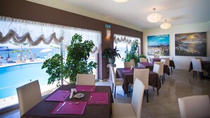A restaurant with tables set for dining, a view of the pool, and potted plants.