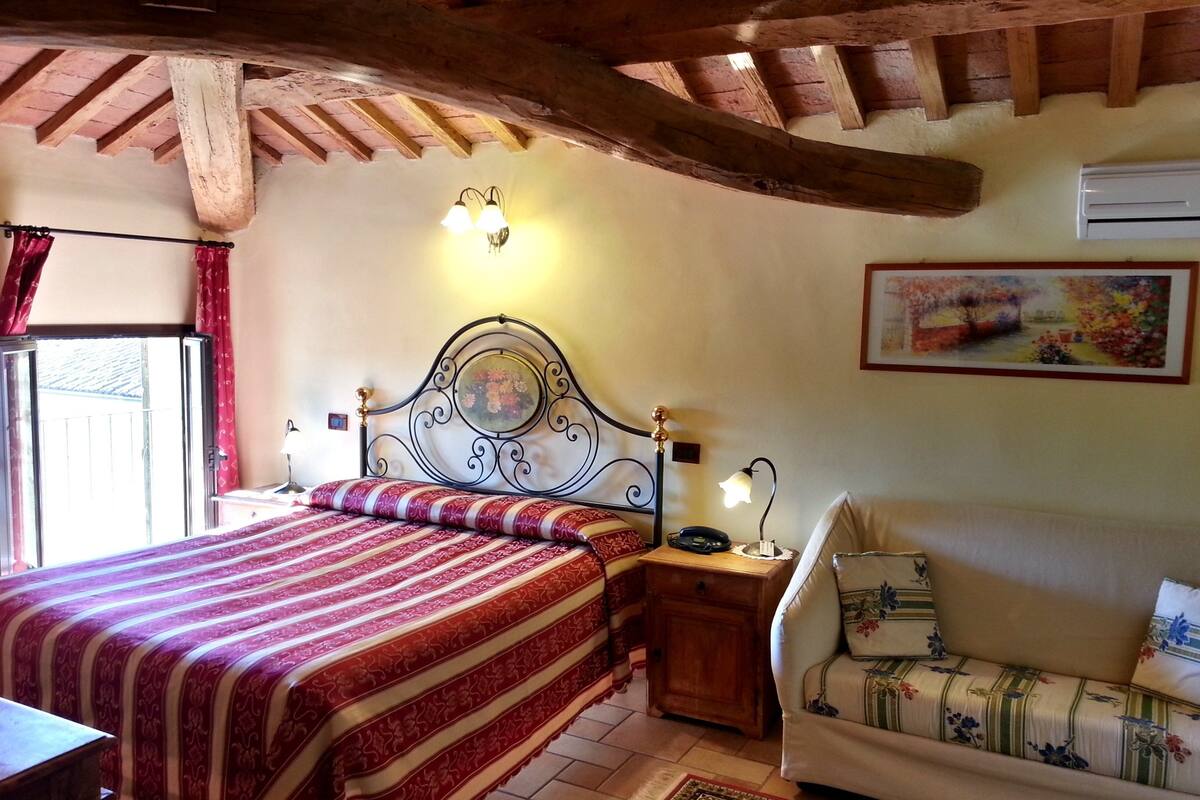 Een slaapkamer met een bed, nachtkastje, bank, schilderij en raam met gordijnen.