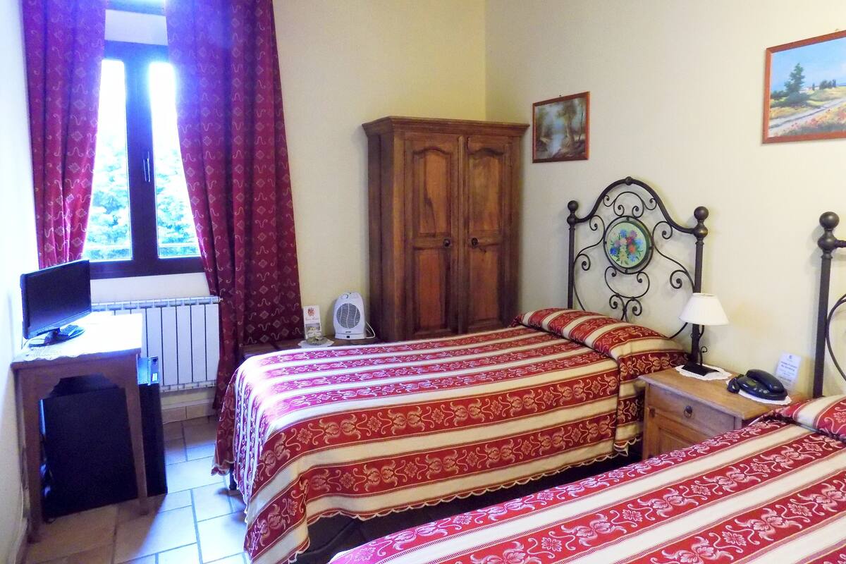 Een slaapkamer met twee bedden, een houten garderobe, een bureau met een computer en een raam met gordijnen.