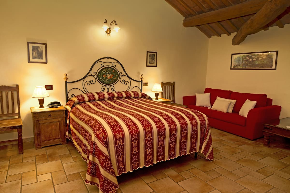 Een slaapkamer met een groot bed, twee nachtkastjes met lampen, een rode bank en ingelijste foto's aan de wand.