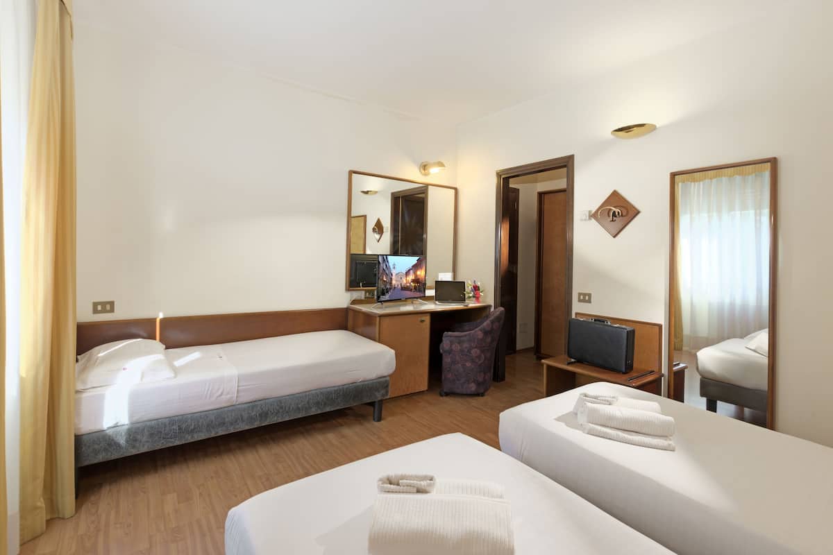 A hotel room with two single beds, a desk with a computer, a chair, and a TV.