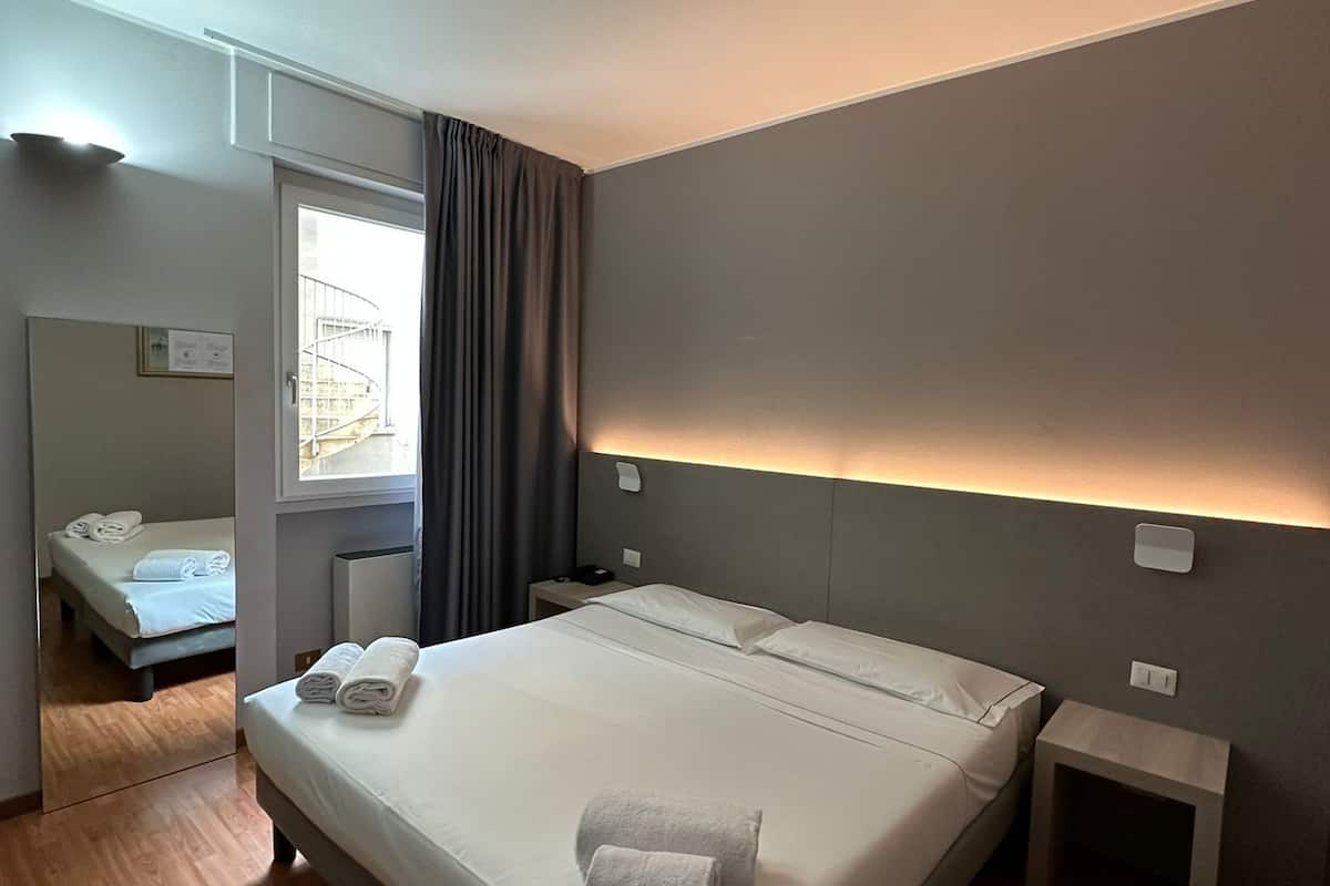 A modern hotel room with a large bed, a bedside table, a mirror, and a window with curtains.