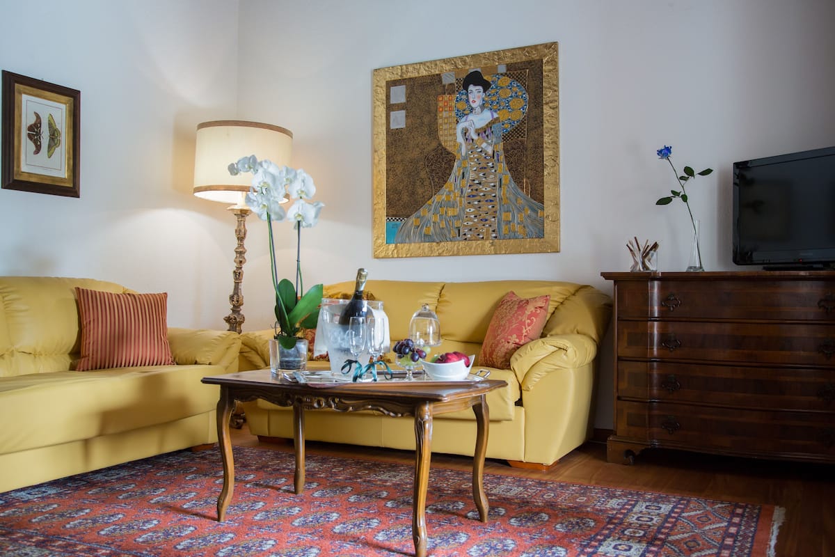 A living room with a yellow sofa, a wooden coffee table, a lamp, a painting, and a television.
