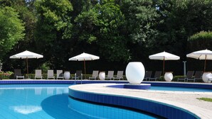 A swimming pool with blue tiles, surrounded by lounge chairs and white umbrellas. - Hotel Villa Condulmer (Mogliano Veneto)