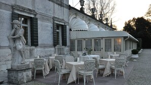 An outdoor dining area with tables and chairs, a statue, and a building facade. - Hotel Villa Condulmer (Mogliano Veneto)