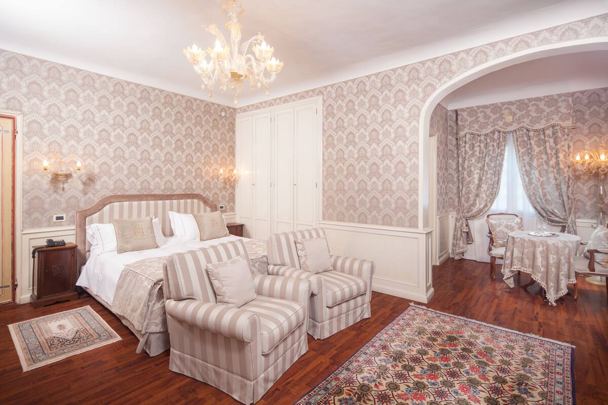 A bedroom with a large bed, two armchairs, a small table, and a chandelier.