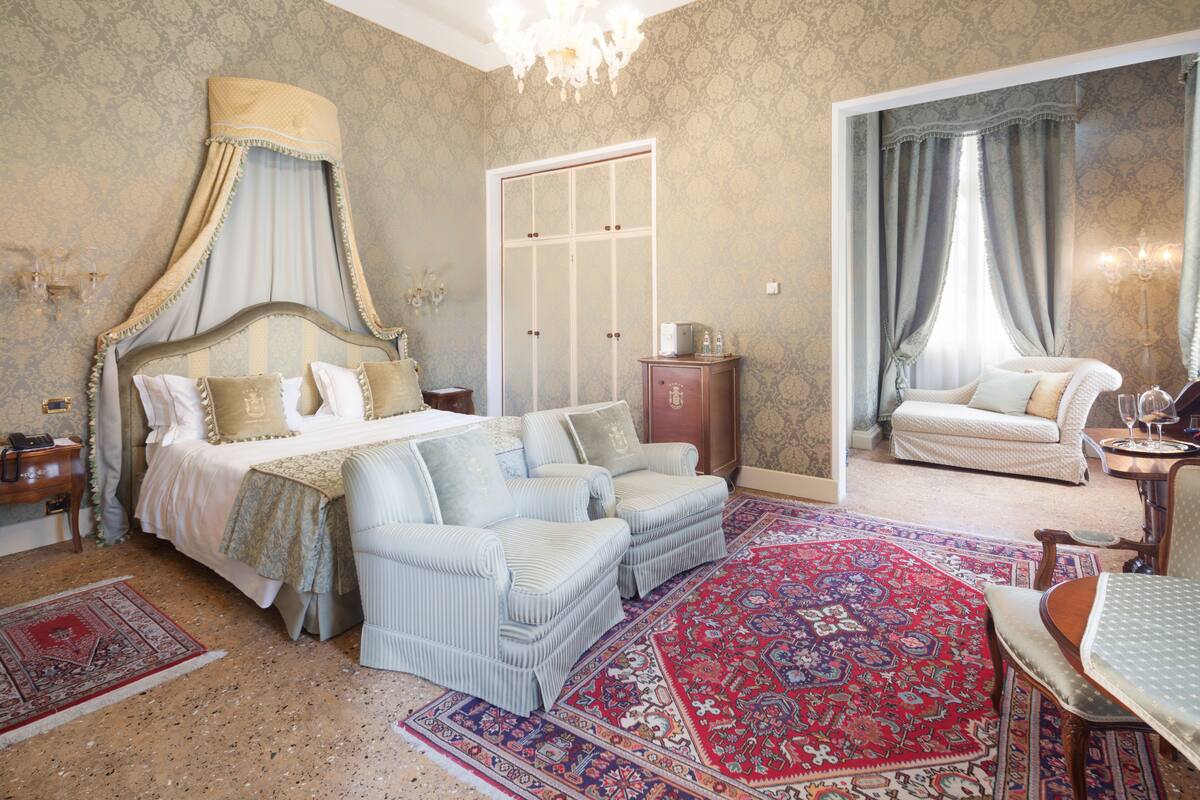 A bedroom with a four-poster bed, a sofa, a small table, and a chair.
