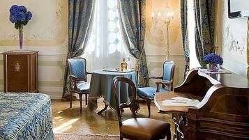 Une chambre à coucher avec un grand lit, un bureau et une chaise. On y trouve une commode et un vase rempli de fleurs posé sur la commode.