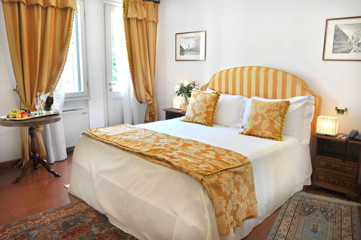 A neatly made bed with a striped headboard, a bedside table with a vase of flowers, and a small lamp.