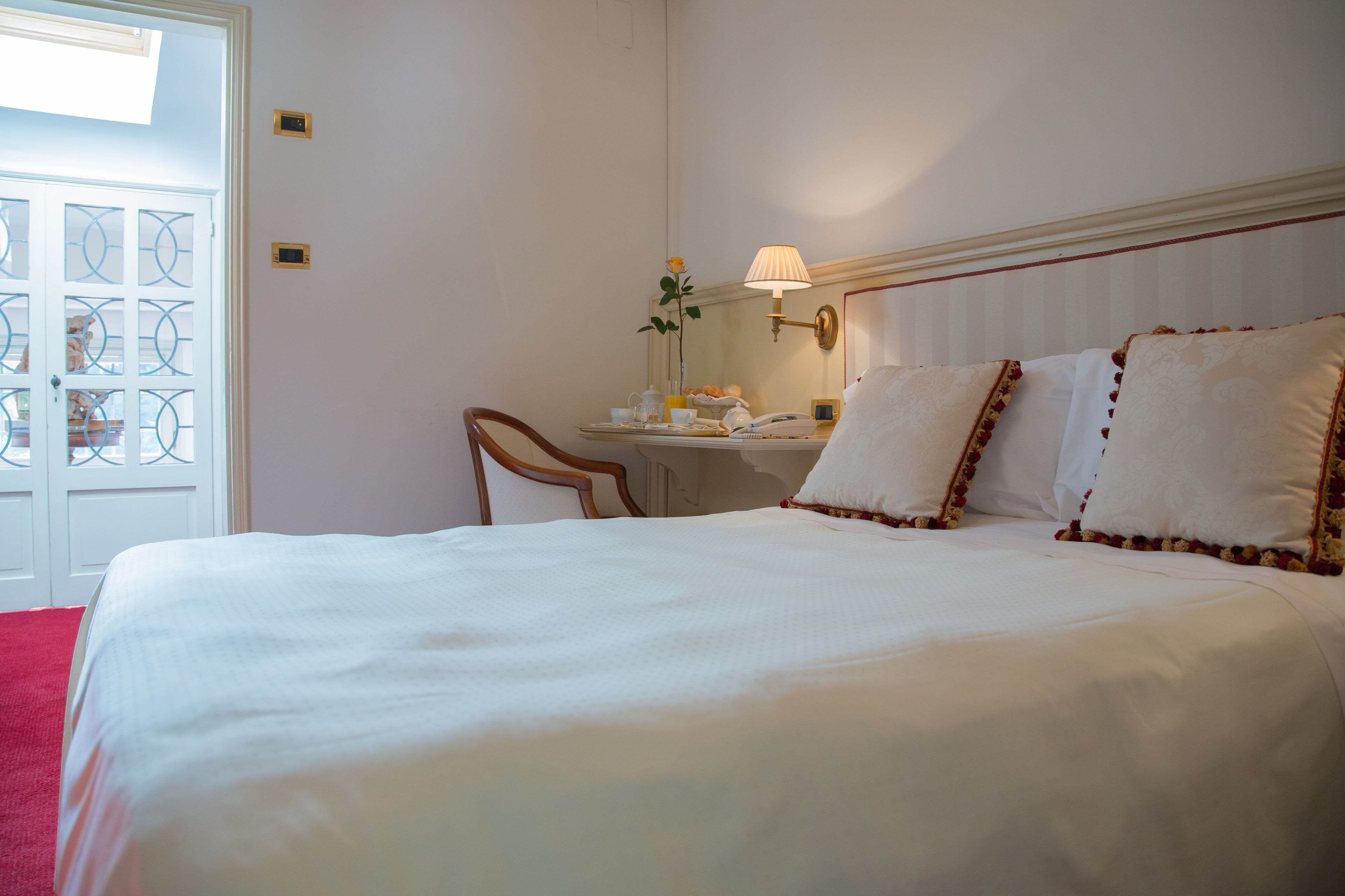A hotel room with a large bed, a desk with a lamp, and a view of a door with glass panels.