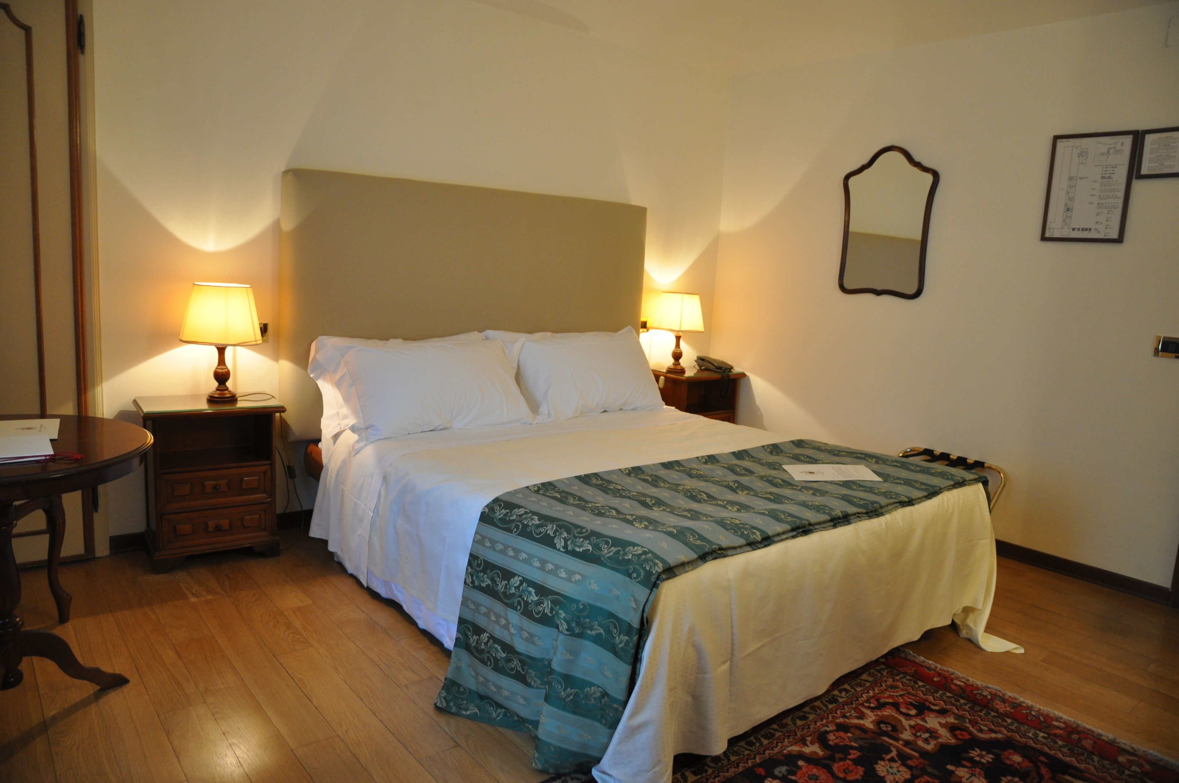 Un lit bien fait, recouvert d’une couvre-lit à motifs, deux lampes de chevet, une table de chevet, une commode en bois et un miroir accroché au mur.