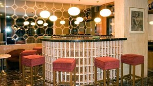 Zona de bar con pared de diseño hexagonal, lámparas colgantes redondas y taburetes con cojines rojos.