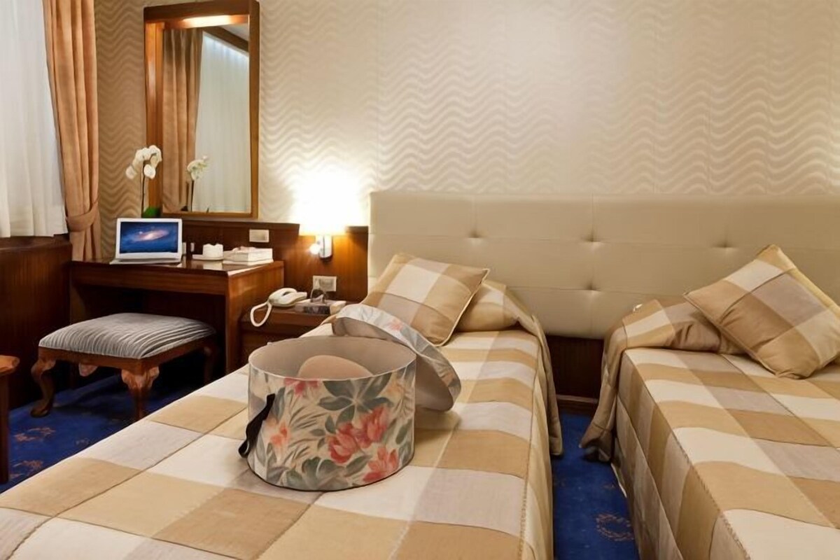 A hotel room with two beds, a desk, a chair, a lamp, and a mirror.