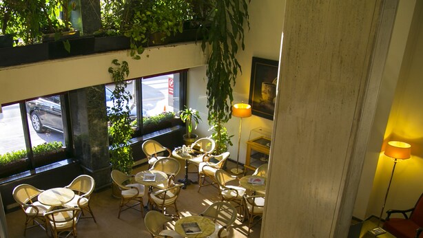 Un espacio interior amplio con varias mesas y sillas, ventanas grandes con vegetación afuera y un techo alto.