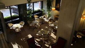 Un amplio espacio interior con varias mesas y sillas, ventanas grandes con plantas y vistas a la calle.