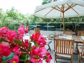 Un patio al aire libre con una mesa preparada para dos personas, rodeado de sillas de madera y un parasol grande.