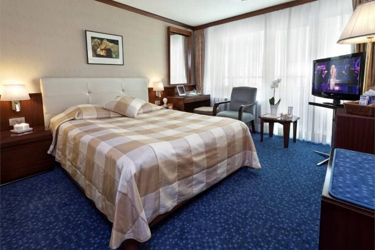 Una habitación de hotel con una cama grande, un escritorio con computadora, un televisor y una silla.