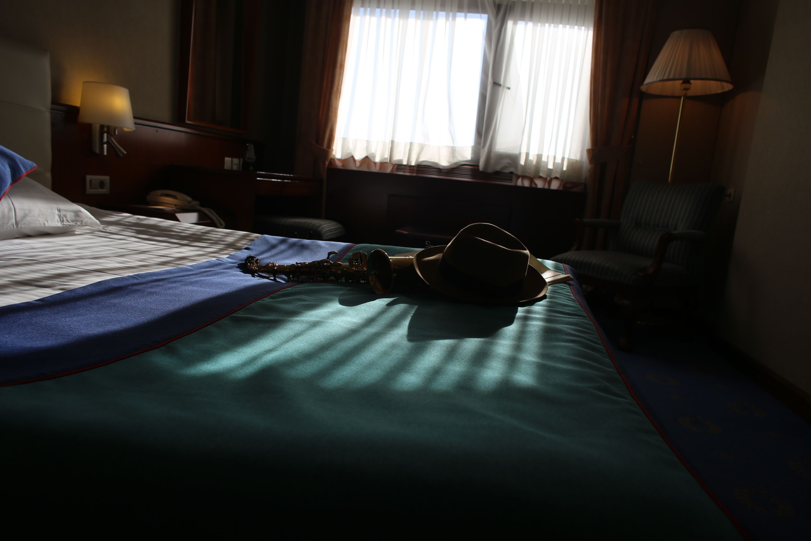 A hotel room with a bed, a chair, a lamp, and a window with curtains.