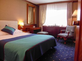 Habitación de hotel con cama, escritorio, silla, lámpara y ventana con cortinas.
