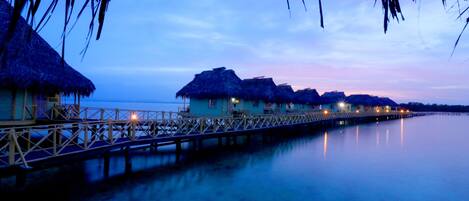A calm waterfront with overwater bungalows connected by a wooden pier.