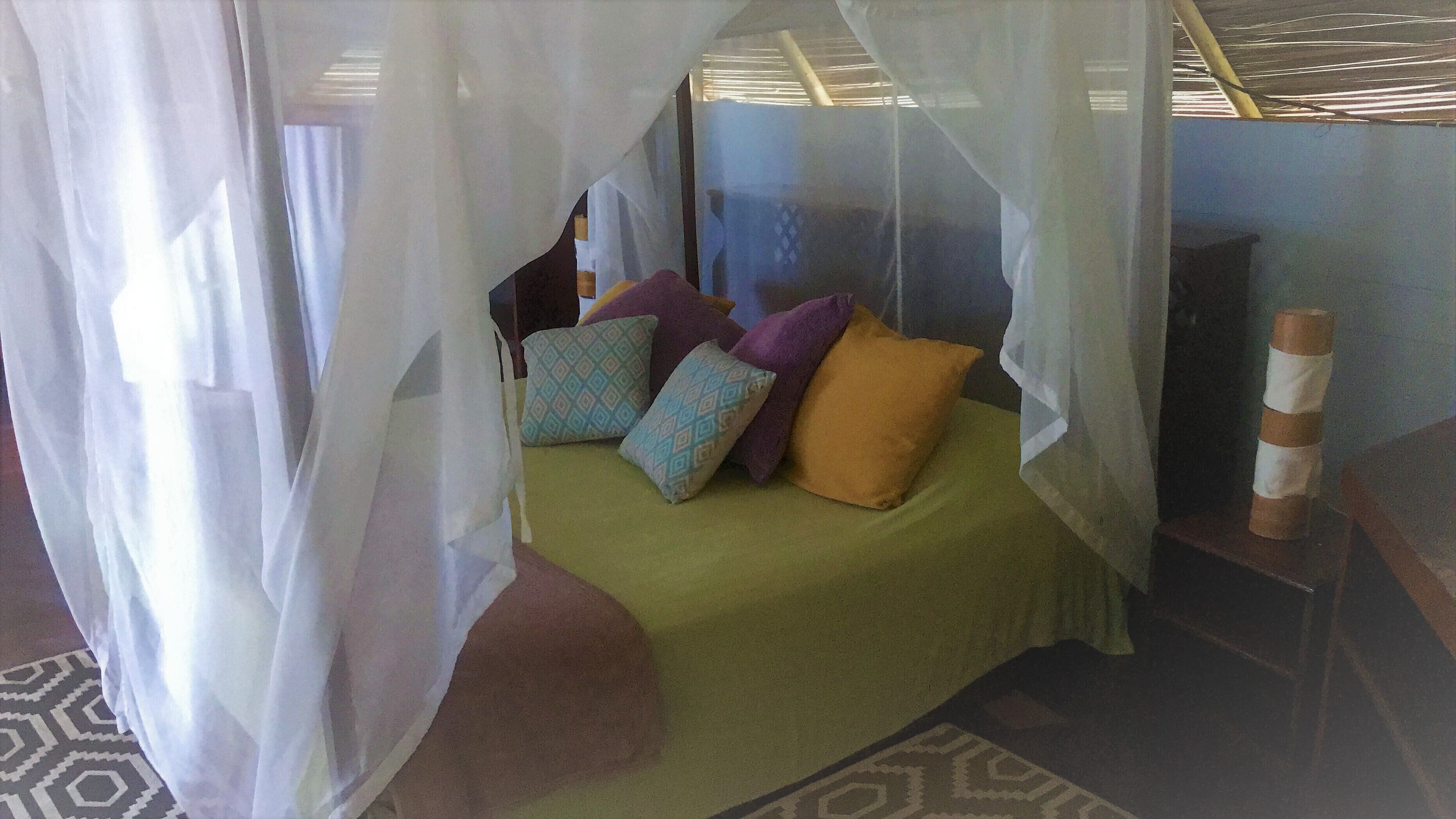Una cama con una colcha verde y almohadas coloridas, un mosquitero y un suelo con estampado.