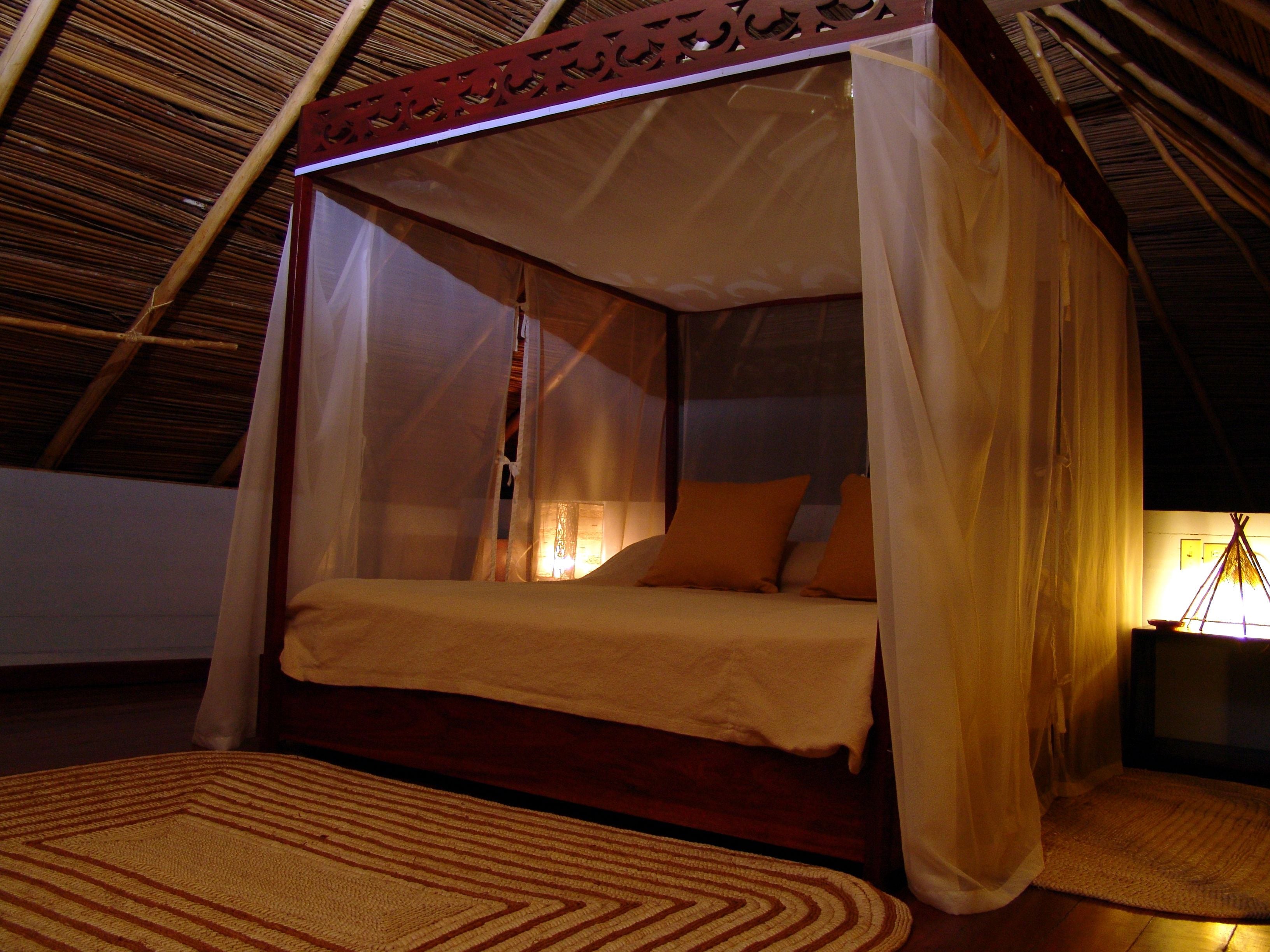 A four-poster bed with a canopy, a wooden floor, and a woven mat.