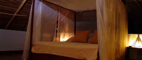 A four-poster bed with a canopy, a wooden floor, and a woven mat.