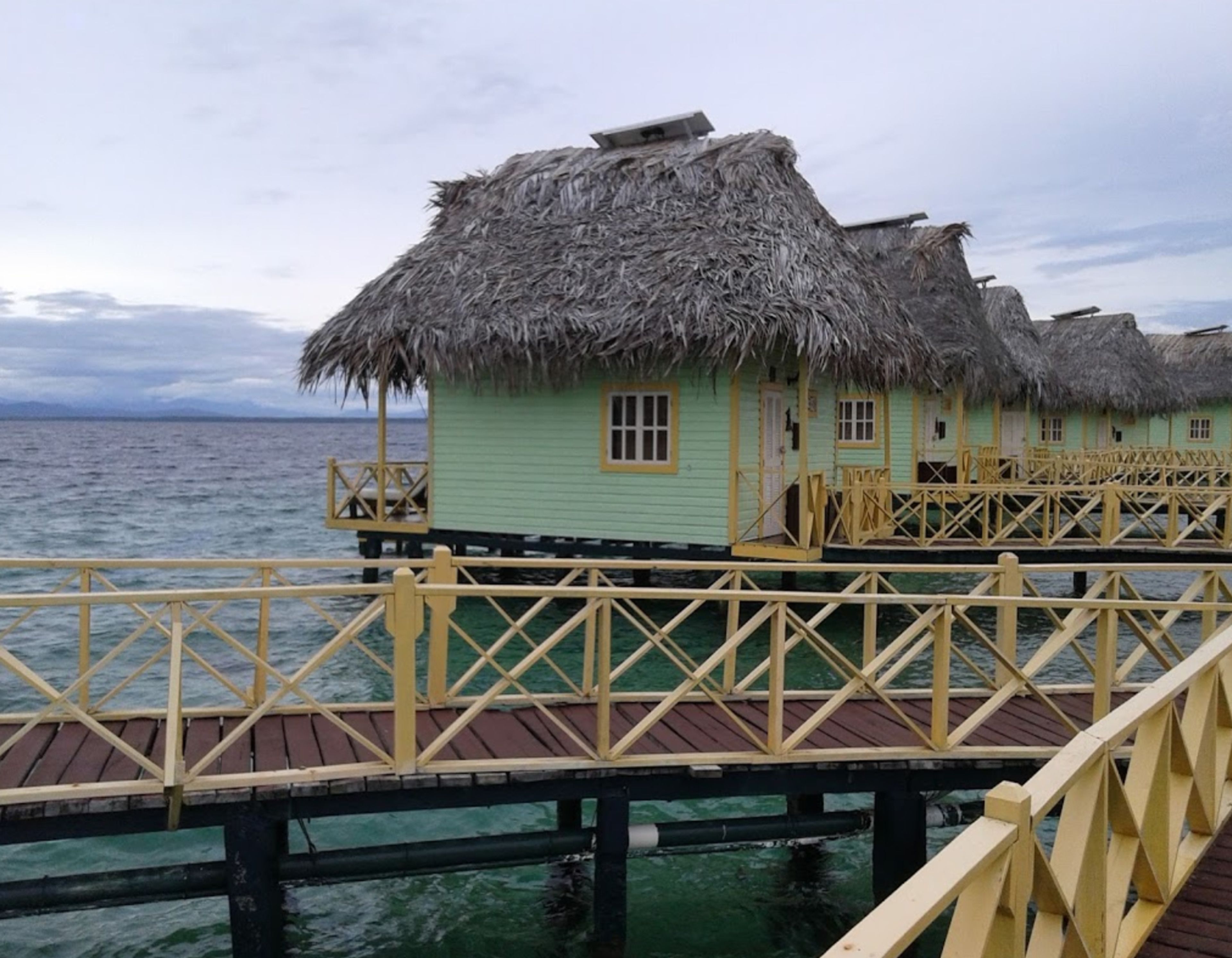 Eine Reihe von überwasserbungalows mit strohgedeckten Dächern, verbunden durch einen Holzsteg.