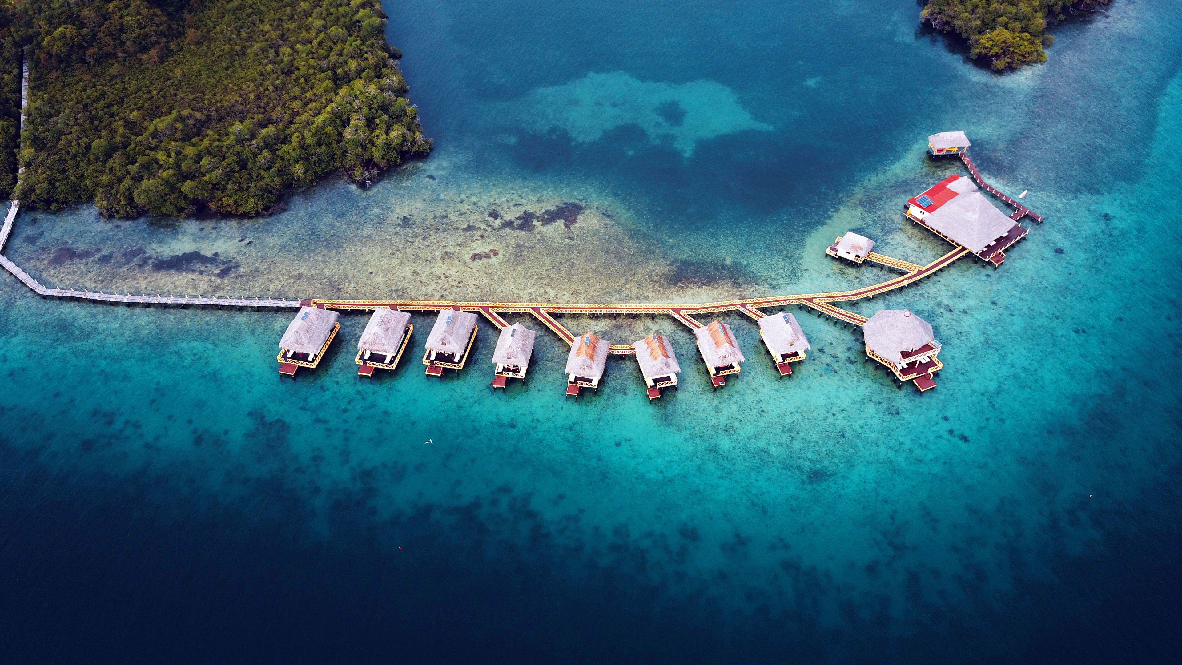 An aerial view of a resort with overwater bungalows connected by a pier.