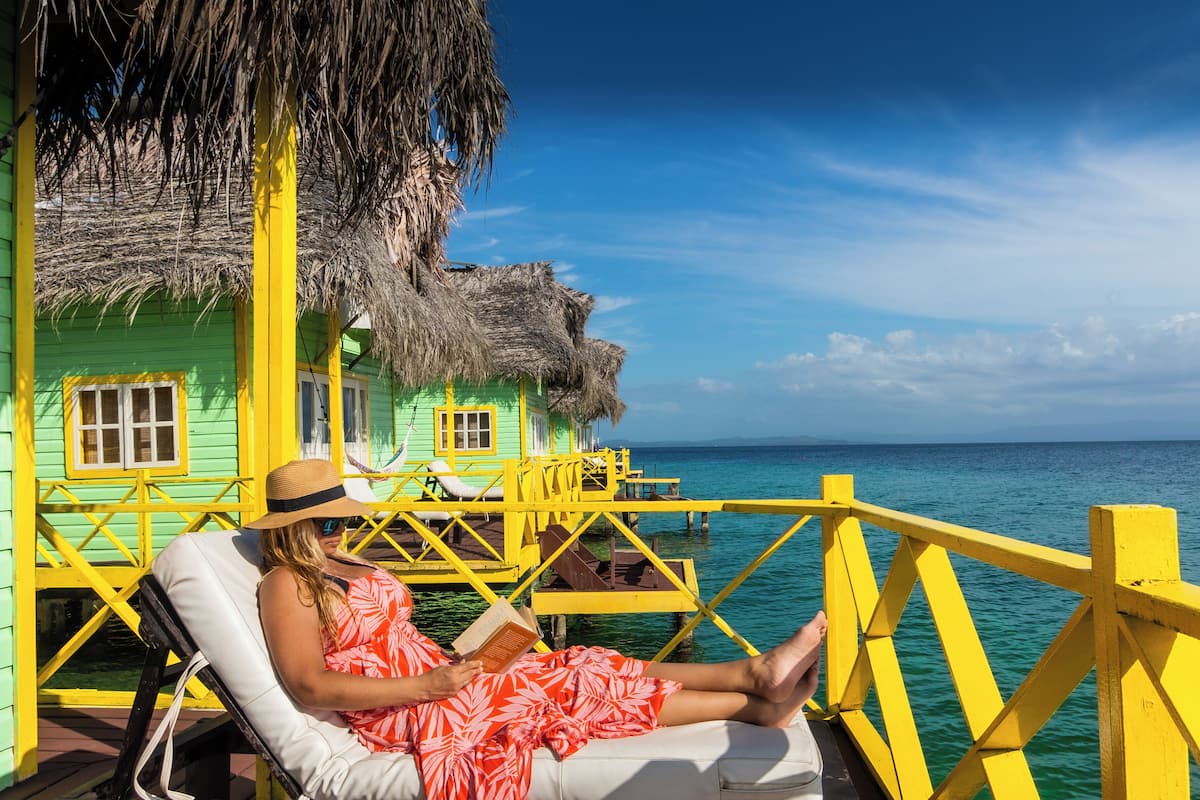 A person relaxing on a yellow deck with a thatched-roof structure in the background.