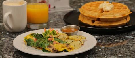 A breakfast plate with eggs, potatoes, and greens, a waffle stack, a glass of orange juice, and a coffee cup.