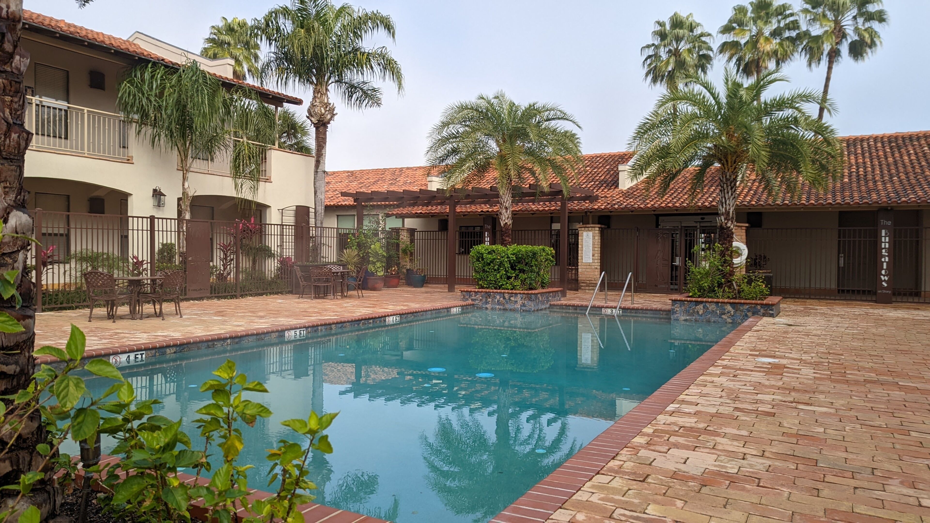 A pool area with a tiled deck, palm trees, and a building with a tiled roof.