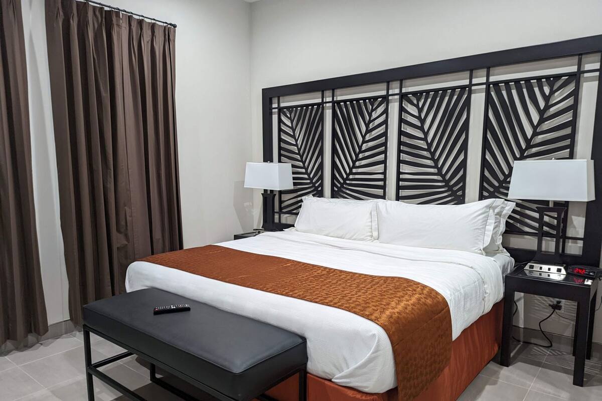 A hotel room with a bed, bedside tables, a nightstand, a remote control, and a window with curtains.