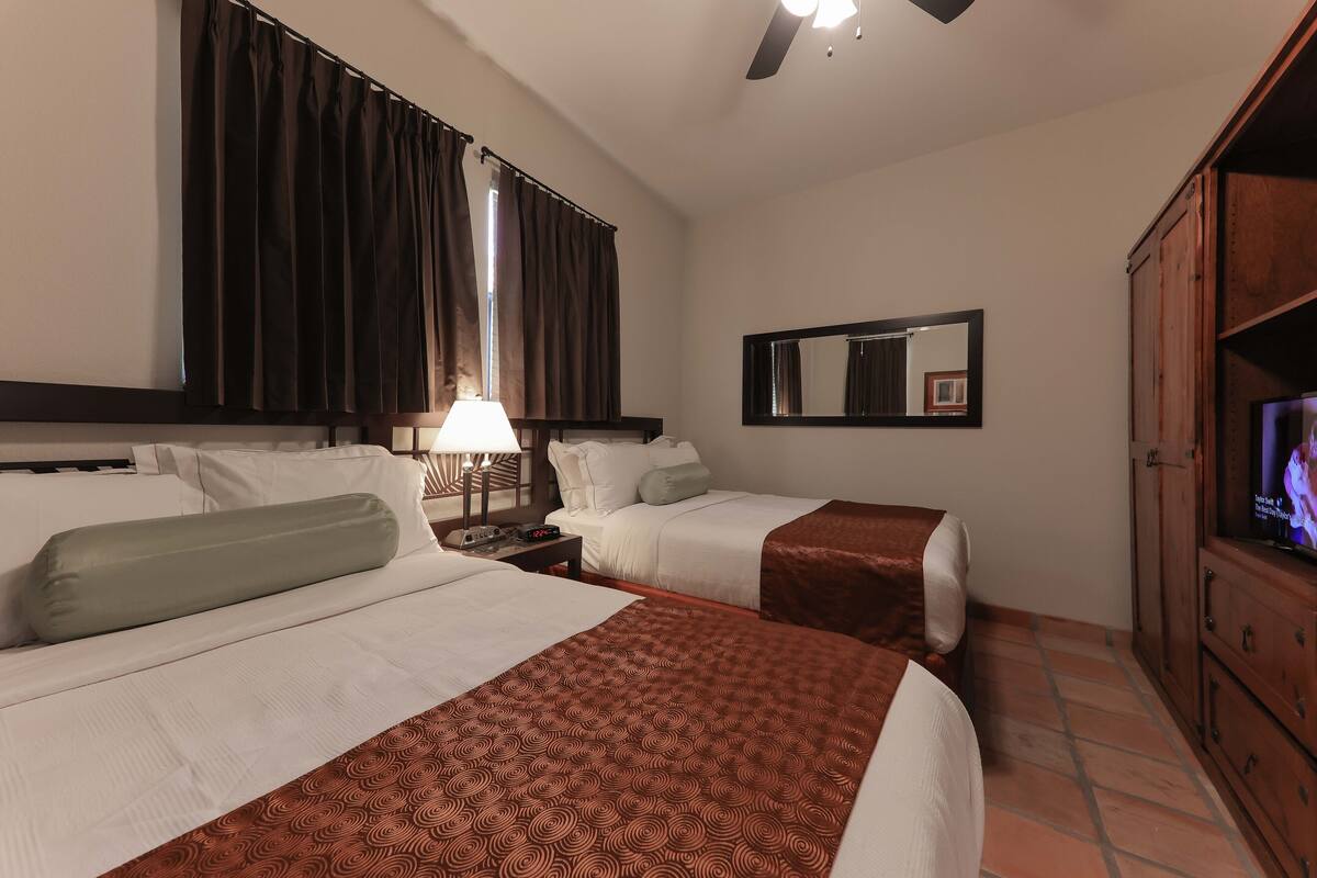 A hotel room with two beds, a TV, a mirror, and a wooden cabinet.