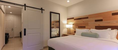 Une chambre d’hôtel comprenant un lit, une table de chevet, un miroir, un ventilateur de plafond et une porte coulissante donnant sur une autre pièce.