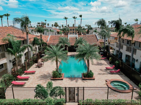 A rooftop pool area with a central swimming pool, lounge chairs, and palm trees.