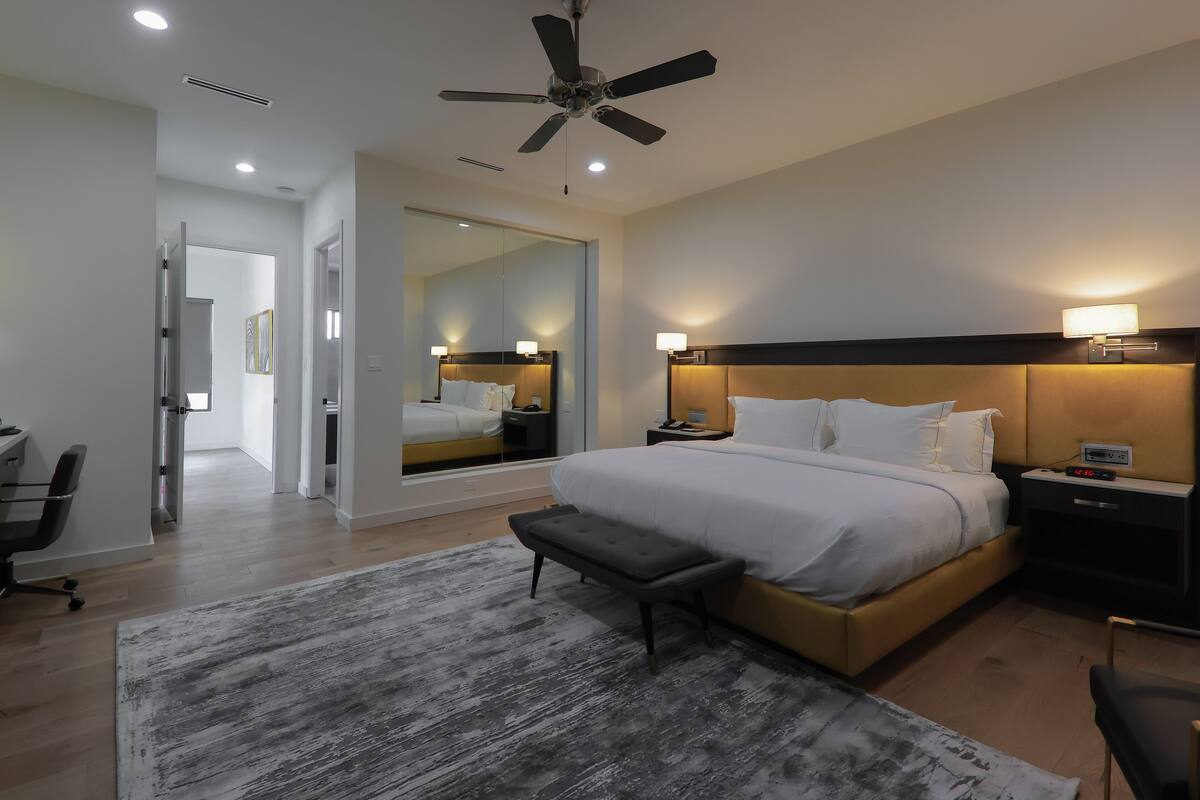 A modern hotel room with a large bed, bedside tables, a desk, and a ceiling fan.