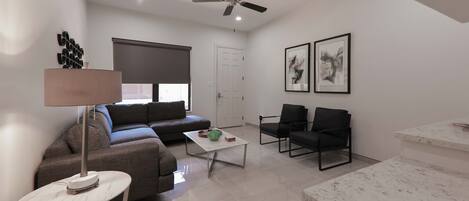 A modern living room with a sofa, two chairs, a coffee table, a lamp, and artwork on the walls.