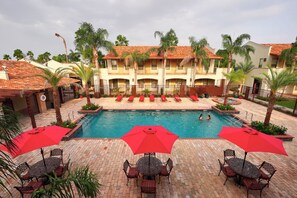 A pool area with red umbrellas, lounge chairs, and a building with a tiled roof. - The Bungalows on Shary, Mission-McAllen (Mission)