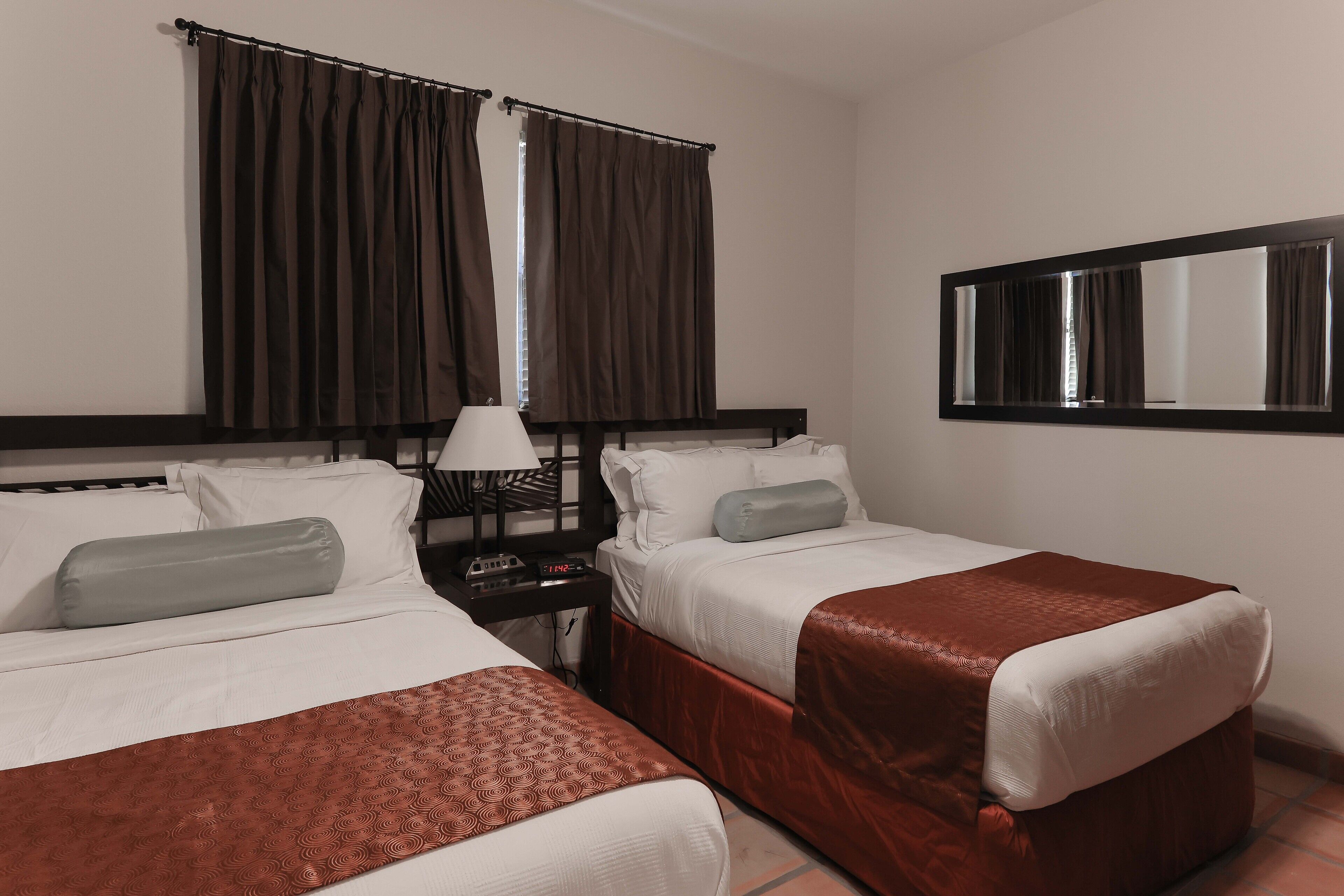 A hotel room with two beds, a nightstand, a lamp, and a large mirror.