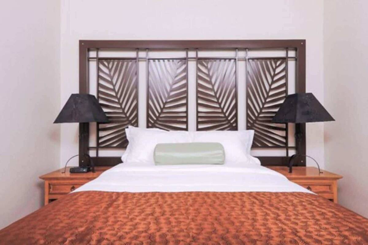 A hotel room with a bed, two bedside tables, and a headboard with a leaf pattern.