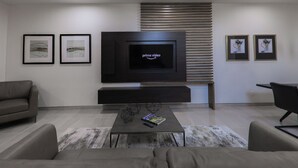 A modern living room with a flat-screen TV, two framed artworks, a sofa, a coffee table, and a black chair. - The Bungalows on Shary, Mission-McAllen (Mission)