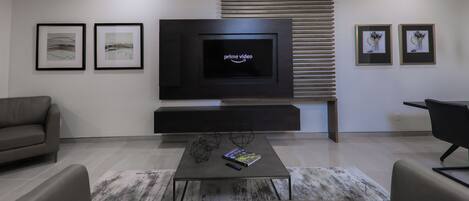 A modern living room with a flat-screen TV, two framed artworks, a sofa, a coffee table, and a black chair.